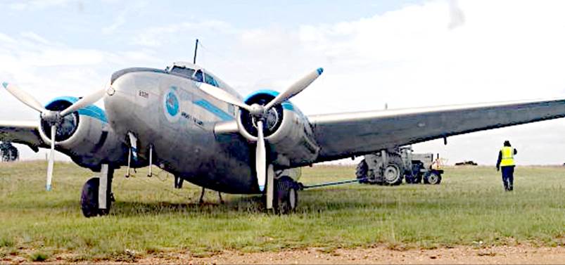 A plane on grass with a few vehicles in the background

Description automatically generated