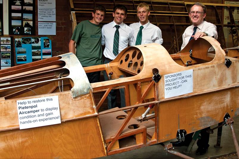 A group of men standing next to a wooden airplane

Description automatically generated