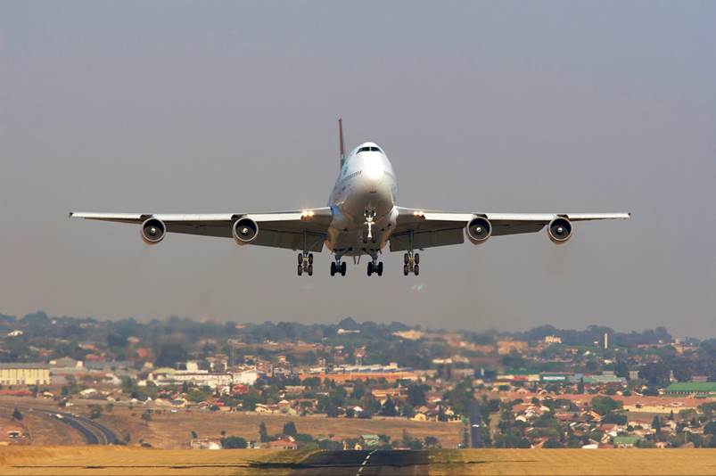 A large passenger jet flying over a city

Description automatically generated