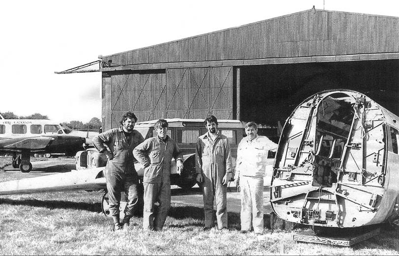 A group of men standing in front of a hangar

Description automatically generated