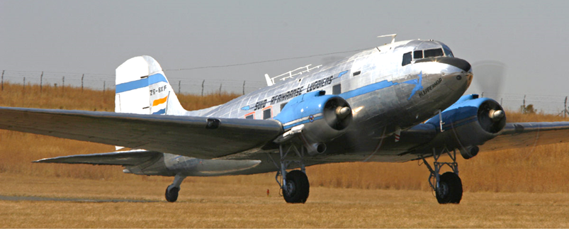 A silver and blue airplane on a field

Description automatically generated