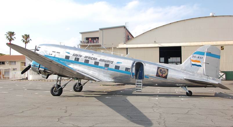 A silver airplane parked in front of a hangar

Description automatically generated